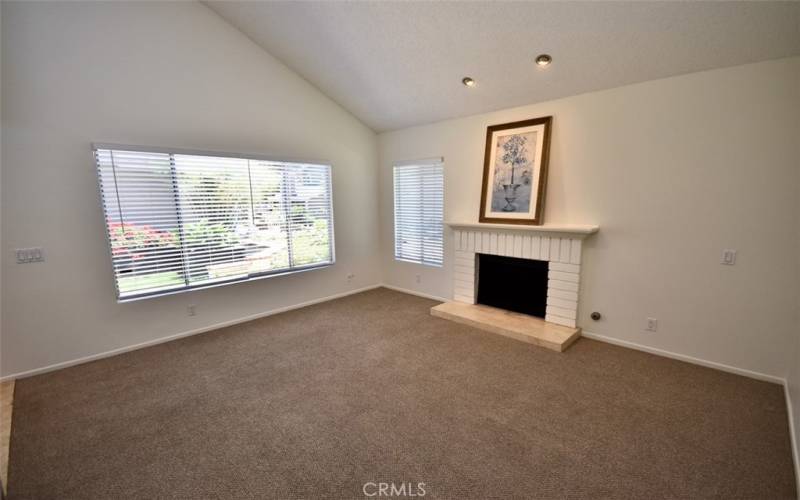 Soft, neutral carpeting in the living room creates a cozy atmosphere complemented by a brick fireplace and oversized windows.