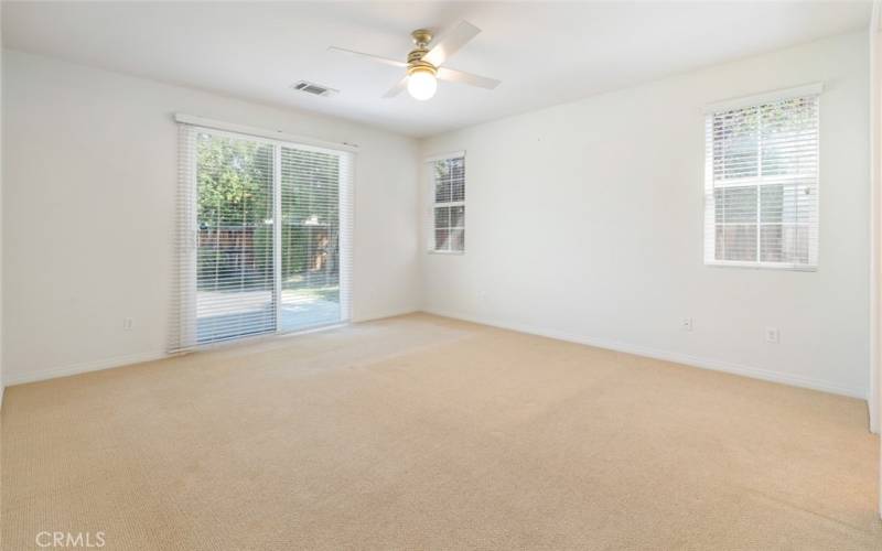 The spacious primary bedroom has private access to the backyard, a ceiling fan with light and carpet flooring.