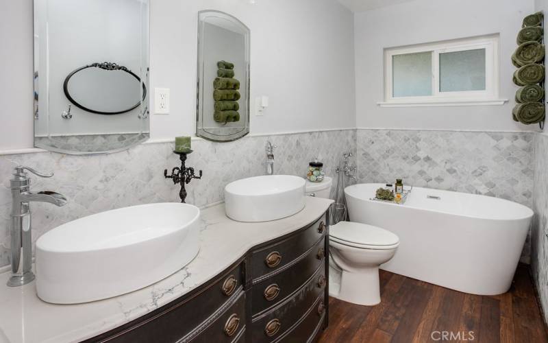  Remodeled main bathroom with custom-made antique quartz crowned vanity, dual vessel bowl basins, modern lighting, large free-standing soaking tub, 4 ft. high marble tile wainscoting, privacy window and newer high-end wood laminate floors.