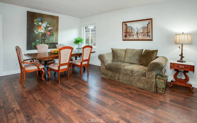 The living room is bathed in natural light from a large glistening window and is further enhanced by newer plantation shutters and newer high-end wood laminate floors.