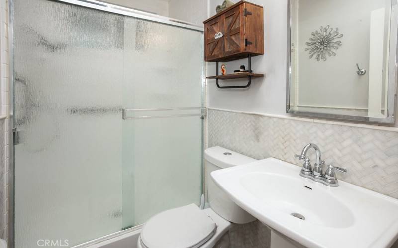 Remodeled guest bathroom with pedestal sink, chic modern lighting, glass-enclosed subway style fiberglass step-in shower, 4 ft. high marble tile wainscoting, privacy window and newer high-end wood laminate floors.