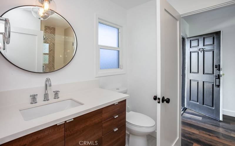 Remodeled guest bathroom with guest access and guest bedroom access, modern quartz crowned floating vanity, undermount basin, glass globe accent lighting, frameless glass enclosed custom tiled step-in shower, light switch with LED nightlight and fan on timer and tile floors.