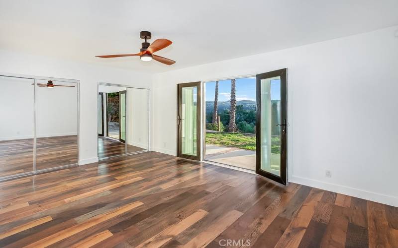 The primary suite is bathed in natural light and is enriched by double French doors that lead to the backyard patio and frame stunning valley views, lighted ceiling fan, dual wall-to-wall closets, mirrored wardrobe doors and gleaming wood laminate floors.