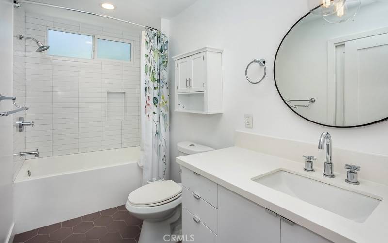 Remodeled en suite bathroom with floating white vanity, quartz countertops, undermount basin, glass globe accent lighting, tiled tub/shower bidet, light switch with LED nightlight and fan on timer and custom hexagonal tile floor.