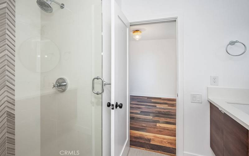 Remodeled guest bathroom with guest access and guest bedroom access, modern quartz crowned floating vanity, undermount basin, glass globe accent lighting, frameless glass enclosed custom tiled step-in shower, light switch with LED nightlight and fan on timer and tile floors.