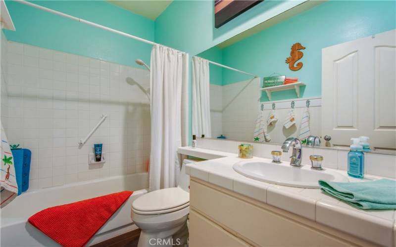 Second full bath with bright white shower and tub tile, bright white counter tile and single sink.