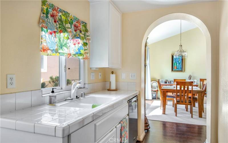 Beautiful archway entry into kitchen, including bright white tile countertops, dual sinks and dishwasher.