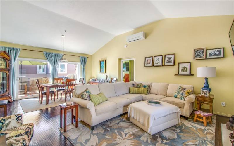 Living room and dining area including padded laminate flooring throughout, vaulted ceiling, recessed lighting, split AC unit and dual pane slider to large back patio.