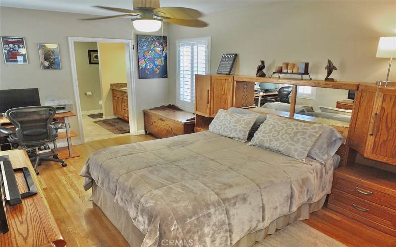 Spacious primary bedroom with an ensuite bathroom and beautiful wood flooring and and a lighted ceiling fan.