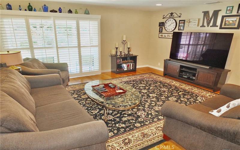 Welcome to a warm and inviting living room with beautiful wood flooring. The sliding glass door, adorned with elegant shutters, opens to a charming backyard porch, creating a seamless indoor-outdoor living experience.