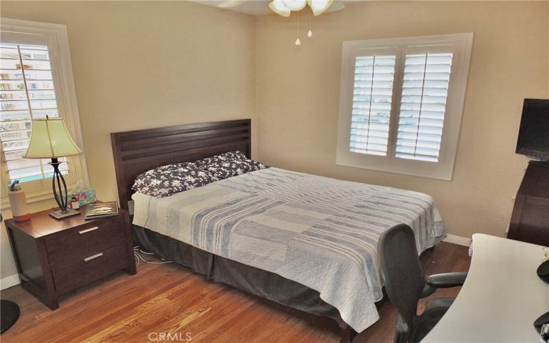 Another perspective of the second bedroom, showcasing both windows with shutters and a ceiling fan with lights.