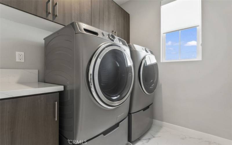 LAUNDRY ROOM WITH BUILT-IN UPPER CABINETRY. FRONT LOAD WASHER/ DRYER WITH LAUNDRY PEDESTALS.