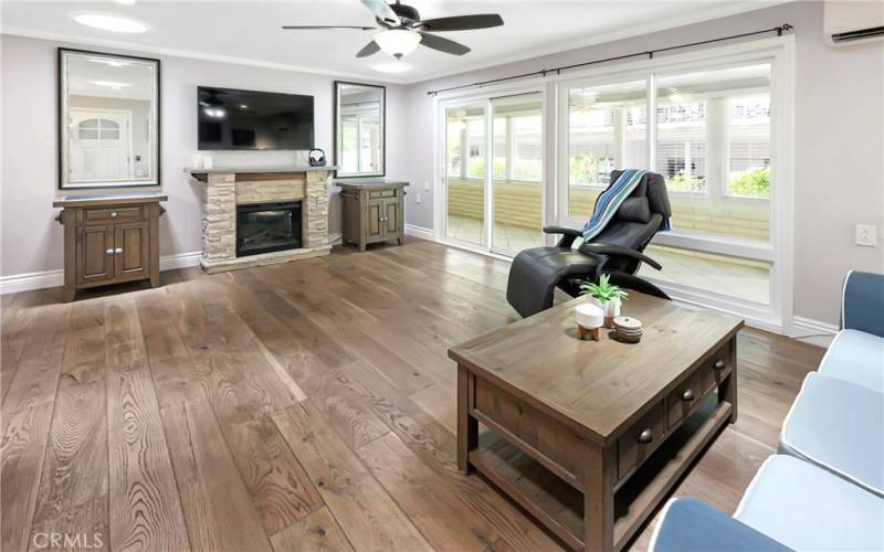 Open concept living space with engineered wood floors, ceiling fan, electric fireplace and attached sunroom