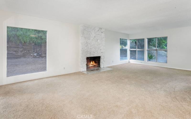 The living room is bathed in natural light from a multitude of windows and is enhanced by a floor-to-ceiling stone fireplace, sliding glass doors that lead to the backyard and new wall-to-wall carpet.