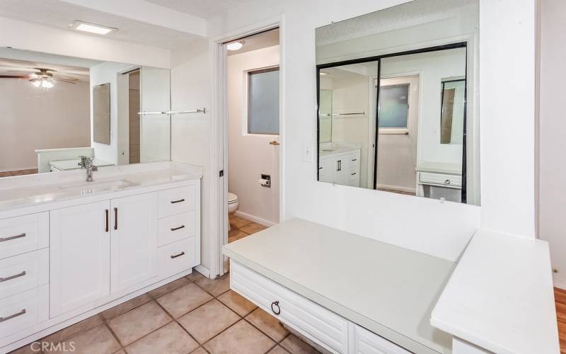 Freshly painted private en suite primary bathroom with white vanity, stone countertop, newer undermount basin, large dressing mirror, built-in make-up vanity, and privacy area with tiled step-in shower, commode and tile floors.