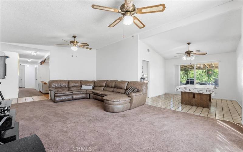 Formal living room and dining have ceiling fans. Window view of covered patio/backyard. Throughway from dining to the kitchen. Right of image leads to family room and hallway to bedrooms.