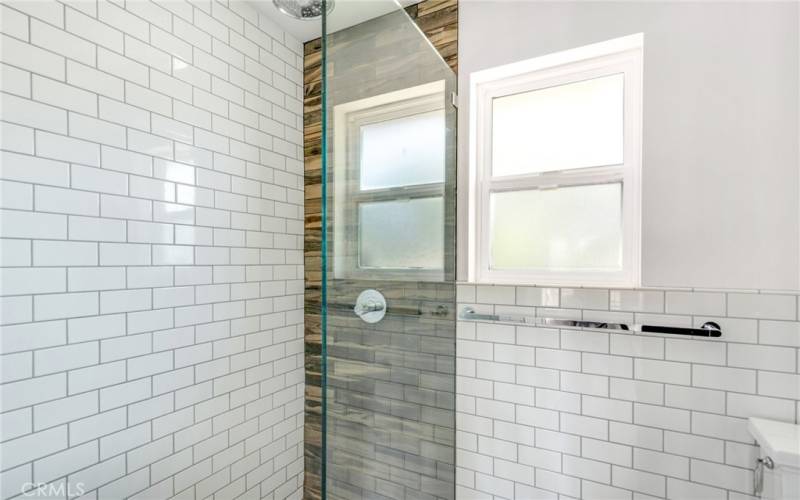 Primary bathroom shower featuring subway tiles, glass splash window and rain shower.