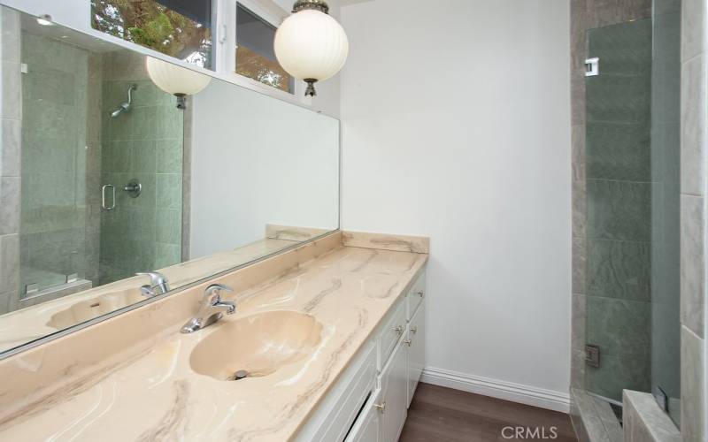 Private en suite primary bathroom with white vanity with integrated basin, large dressing mirror, and frameless glass-enclosed custom tiled step-in shower with bench seat.