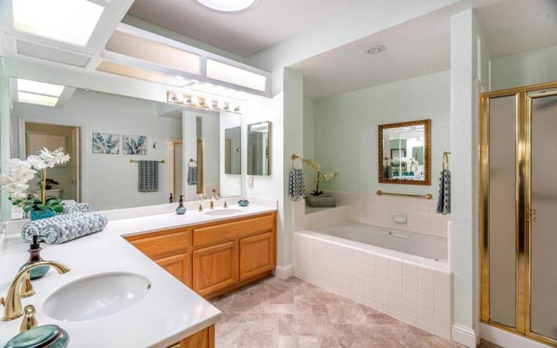 main bedroom bathroom with dual sink, large soaking tub, ceiling skylight and stand-up shower