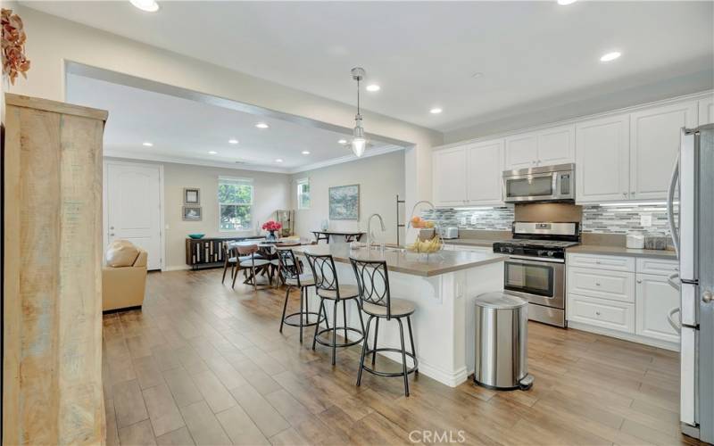 Kitchen with stainless steel appliances, a full mosaic tiled backsplash, quartz countertops, island breakfast bar, custom cabinetry and pendant light