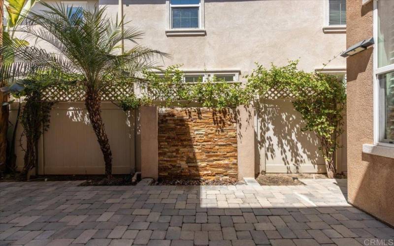 A patio has a rock waterfall against the wall that makes a relaxing trickling sound for outdoor time