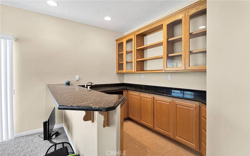 Wet bar with dark granite counters, sink, bar ware display.