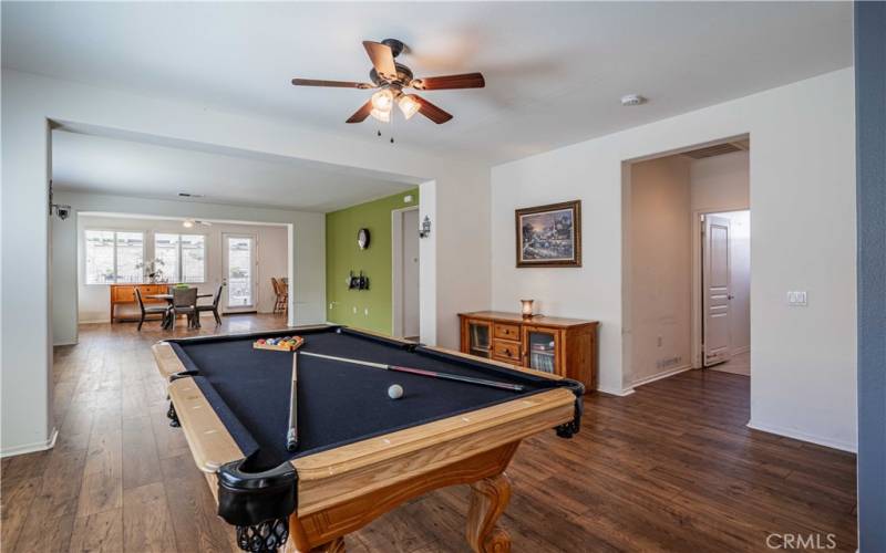 Front room is the pool table room with ceiling fan above, then family room. Back end is the dining room space with ceiling fan above and kitchen in the far right corner. Wood laminate flooring. First doorway on the right leads to the laundry room, and 2 car grage entry.