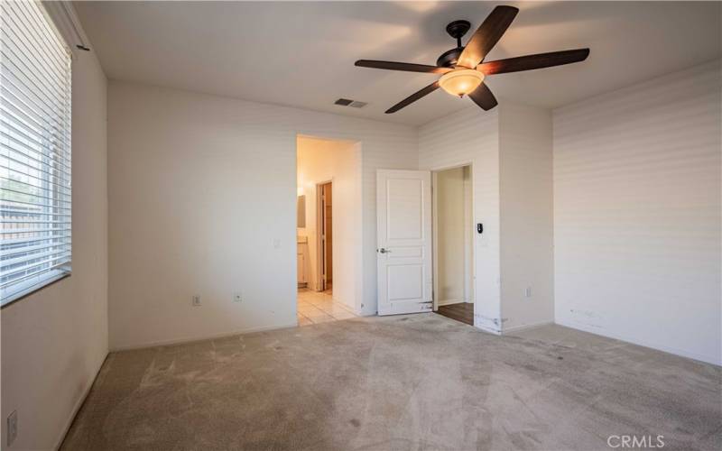 Primary bedroom with ceiling fan and carpet. En-suite bathroom and door to the right leads to the walk-in closet. Tiled bathroom with dual sinks, and privacy toilet room. Tiled  flooring in the bathroom. Carpet in the bedroom.