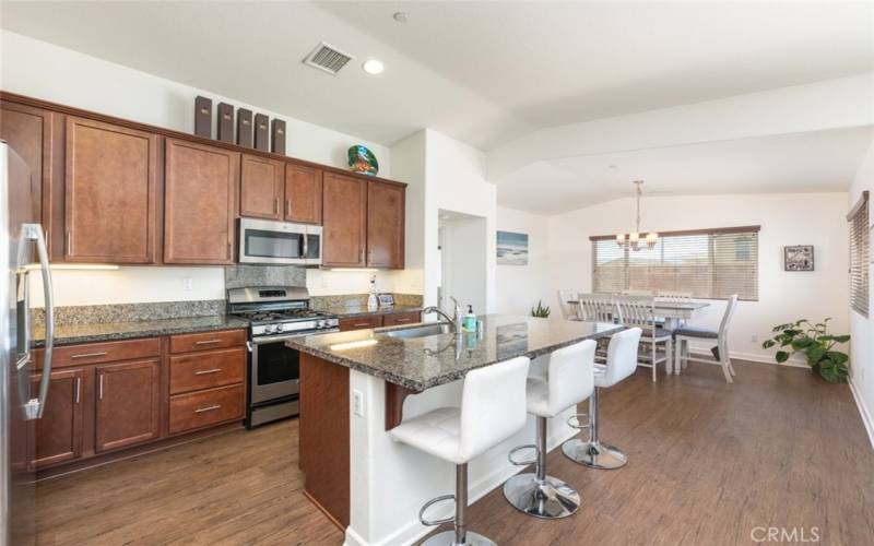 This modern kitchen features rich cabinetry, granite countertops, stainless steel appliances, and an inviting breakfast bar, seamlessly flowing into the adjacent dining area.