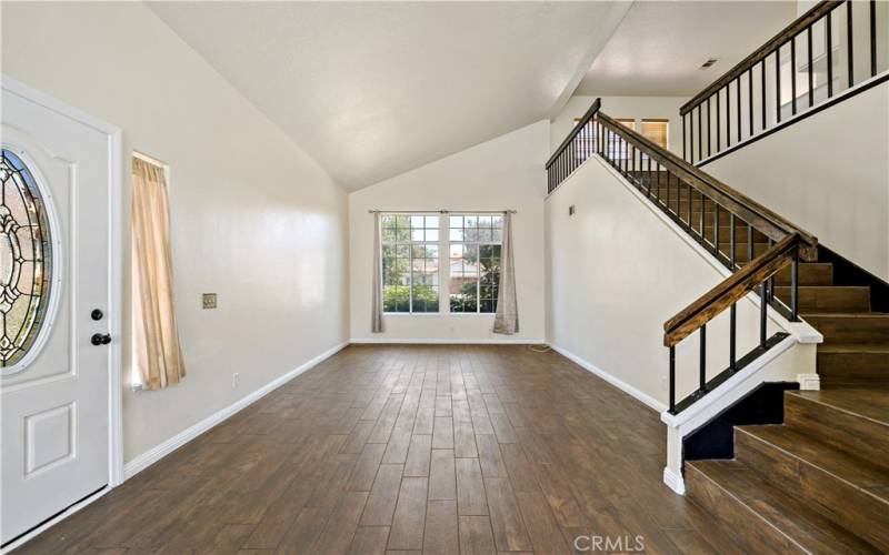 Living room and stairway to second level. plank tile flooring throughout and dramatic vaulted ceilings