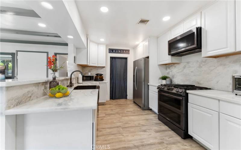 Updated kitchen with marble counters/backsplash, recessed lighting. Indoor laundry in the distance with exterior door to the back patio and another exterior door to the back from the family room.