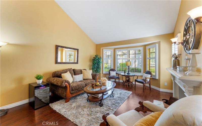 High angled ceiling of formal living room with fireplace. Bay window overlooks the pathway.