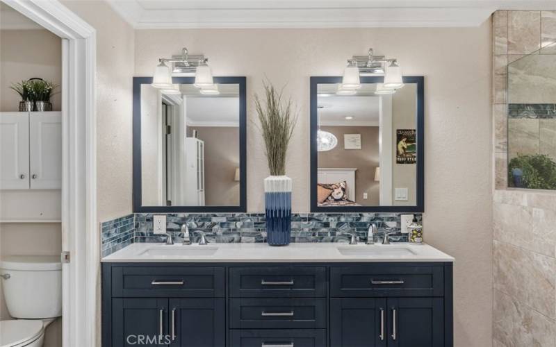 The primary bath features dual sinks, custom shaker cabinetry, natural stone countertops, and designer tile accents. There is also a privacy door and oversized walk-in tile shower.