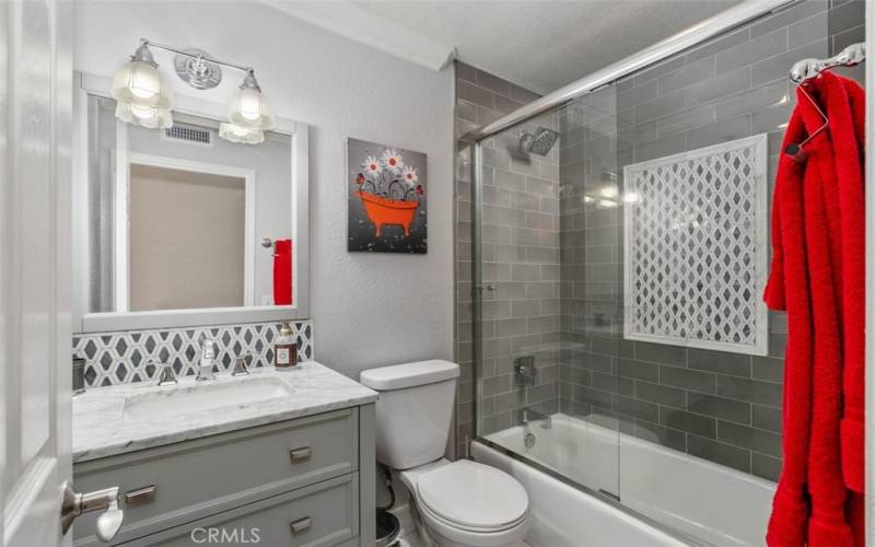 Updated secondary full bath has designer tile, shower/tub combo, custom cabinetry and a natural stone countertop.