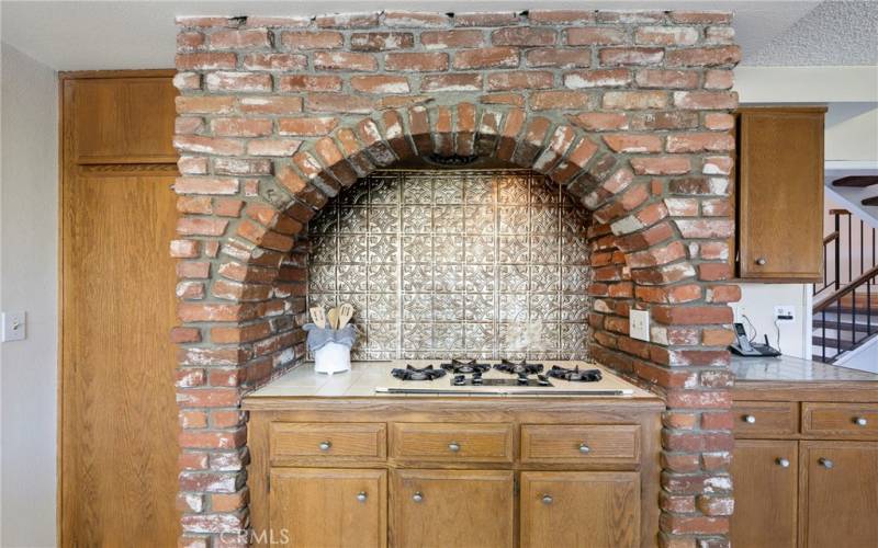 Gas stove top in brick alcove with pantry at left & extra storage cabinetry.