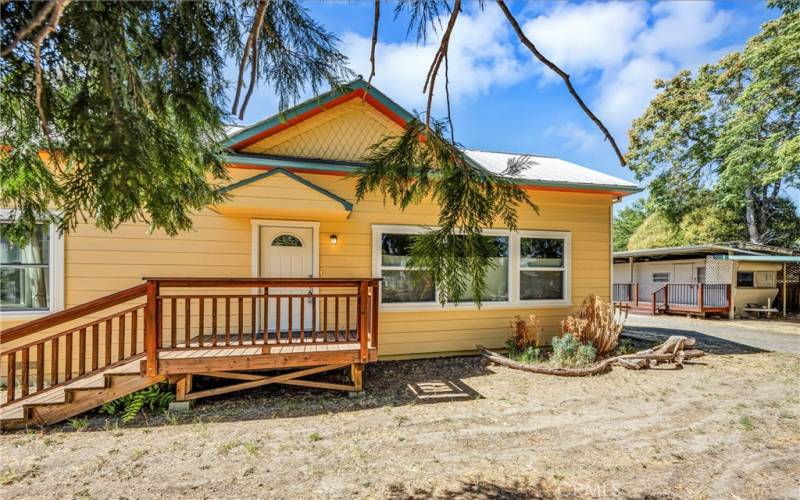 Front of home. Metal and comp roof, grid tie solar, two driveways into the property connected and accessing the 2 car garage, outbuildings and the spacious private yard.  Additionally,  to the right of home is a one bedroom guest trailer on city services with covered parking.