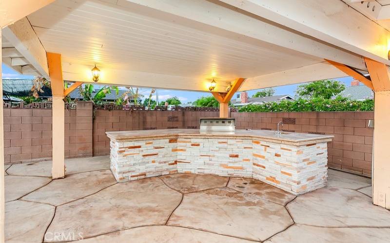 BBQ island with granite countertops, stainless steel basin and refrigerator.