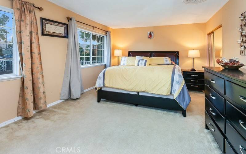 The generously sized primary suite is drenched in natural light from glistening windows and is enriched with dual closets with mirrored wardrobe doors, an additional 2 walk-in closets, and wall-to-wall carpet.