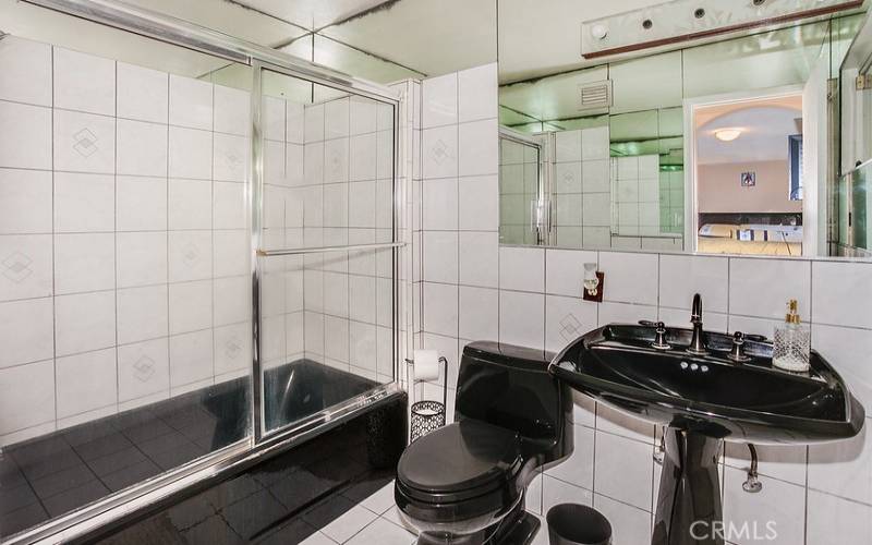 Private en suite full bathroom with pedestal sink, glass-enclosed tiled tub/shower, and tile floors.