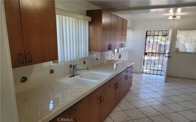 Elegant kitchen with sink, classic quality tile counter  flooring, top quality cabinets, and backdoor with window.