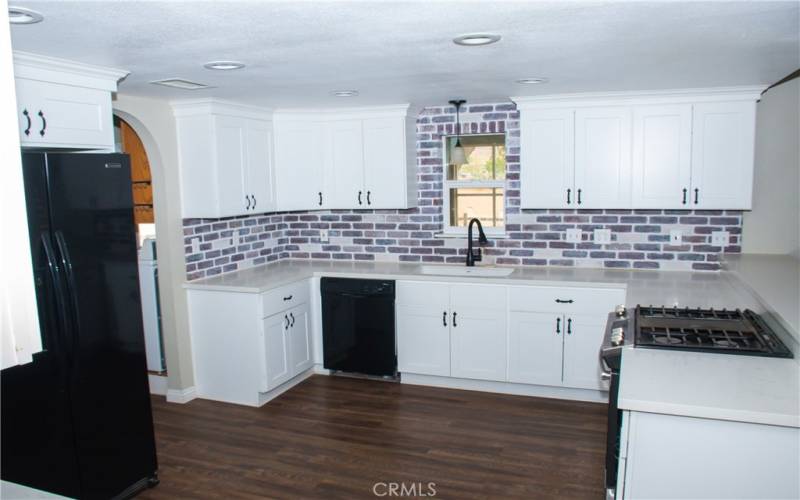 Kitchen with Quartz counters, modern white cabinets, custom backsplash, breakfast bar and stainless/black appliances.