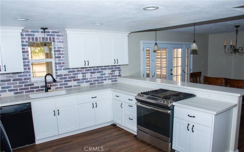 Kitchen with Quartz counters, modern white cabinets, custom backsplash, breakfast bar and stainless/black appliances.