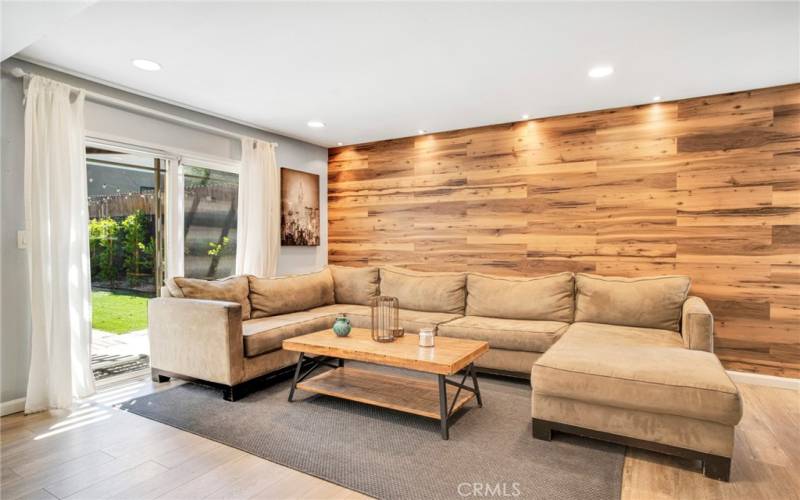 Expansive family room with recessed lights, designer wood-grained accent wall, sliding glass door leading to the backyard and rich wood laminate floors.