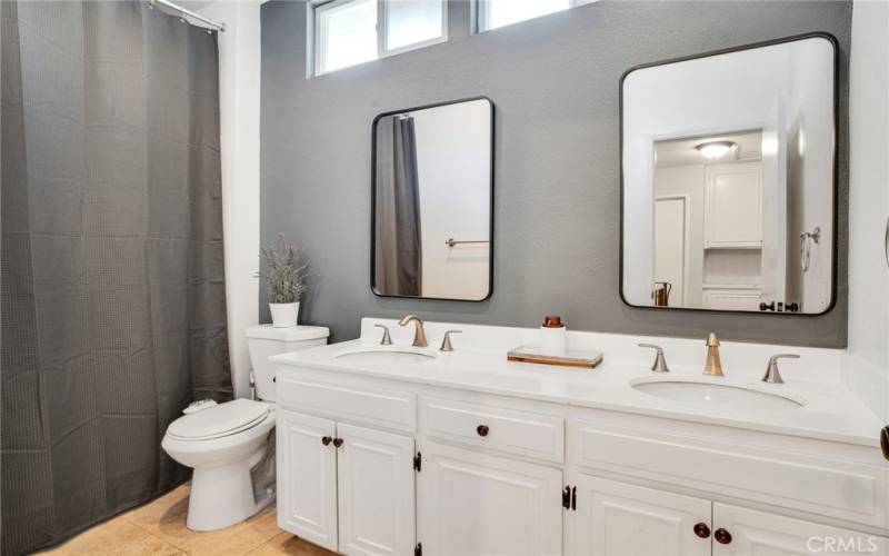 Upstairs full guest bathroom with recessed lights, dual basin white vanity, framed dressing mirrors, glass enclosed tub/shower, bidet and tile floors.