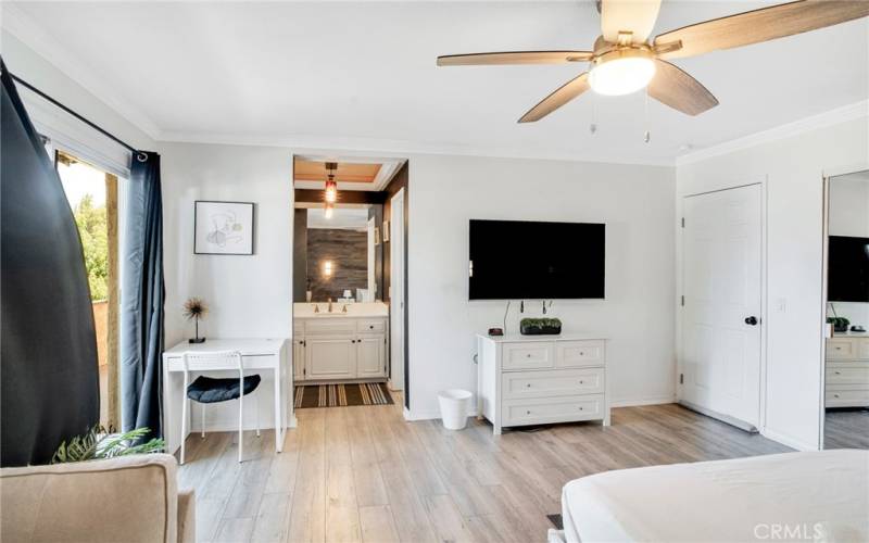 The oversized upstairs primary suite is enriched by crown molding, a lighted ceiling fan, chic wood-grained accent wall with sconce lighting, sliding glass door that leads to a private wrap-around balcony, mirrored wardrobe doors and wood laminate floors.