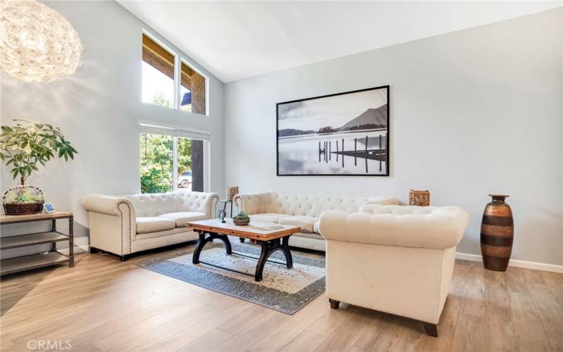 The formal living room bathed in natural light and is enhanced by high pitched ceilings, contemporary drop-down lighting and gleaming wood laminate floors.