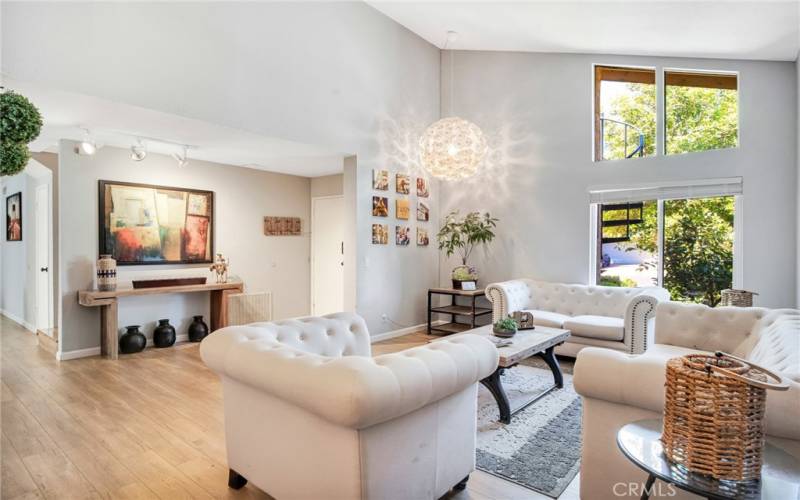 The formal living room bathed in natural light and is enhanced by high pitched ceilings, contemporary drop-down lighting and gleaming wood laminate floors.