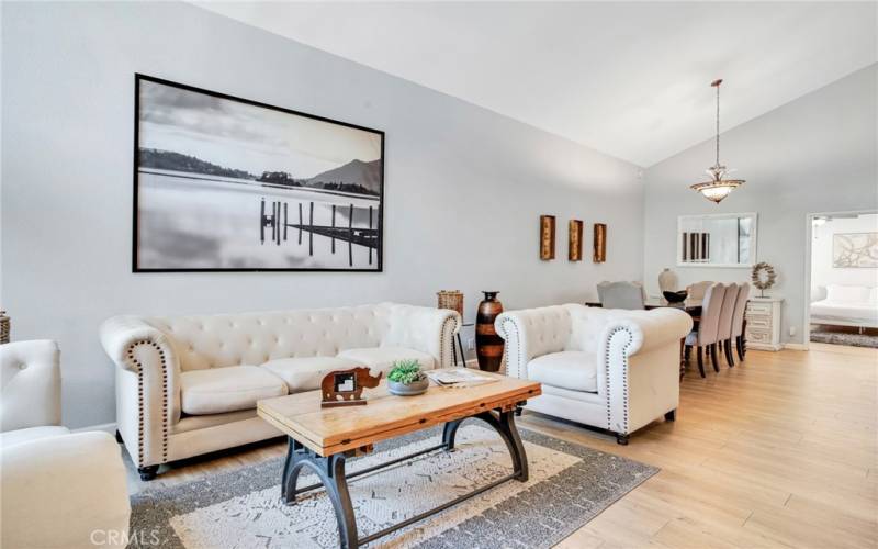 The formal living room bathed in natural light and is enhanced by high pitched ceilings, contemporary drop-down lighting and gleaming wood laminate floors.