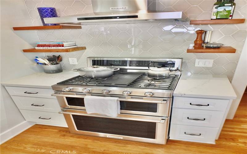 Featuring a gas stove with a built-in grill nestled between exquisite cabinetry, accented by a stylish tile backsplash and a sleek range hood