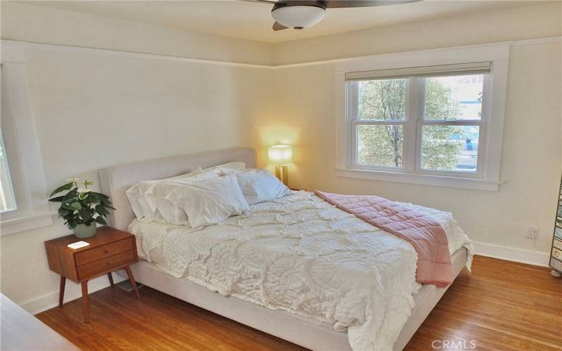 View of the bedroom featuring two windows, elegant picture rail molding, gorgeous wood floors, and a ceiling fan with lights for added comfort